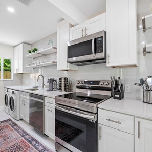 A modern kitchen with stainless steel appliances, white cabinetry, and a built-in oven. - Uhost AI Stylish 1BR Bright Space w Patio (Fort Lauderdale)