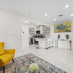 A modern kitchen with white cabinets, stainless steel appliances, and a bar area with stools. - Uhost AI Stylish 1BR Bright Space w Patio (Fort Lauderdale)