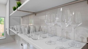 A kitchen with white shelves holding various glassware and a modern faucet. - Uhost AI Stylish 1BR Bright Space w Patio (Fort Lauderdale)