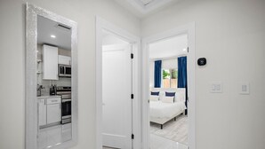 A modern hotel room with a kitchen area, a bed with blue curtains, and a thermostat on the wall. - Uhost AI Stylish 1BR Bright Space w Patio (Fort Lauderdale)