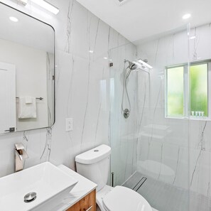 A modern bathroom with a large mirror, white marble walls, a glass shower enclosure, and a window with a view. - Uhost AI Stylish 1BR Bright Space w Patio (Fort Lauderdale)