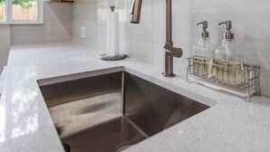 A modern kitchen with a stainless steel sink, a curved faucet, and a soap dispenser holder with bottles. - Uhost AI Stylish 1BR Bright Space w Patio (Fort Lauderdale)