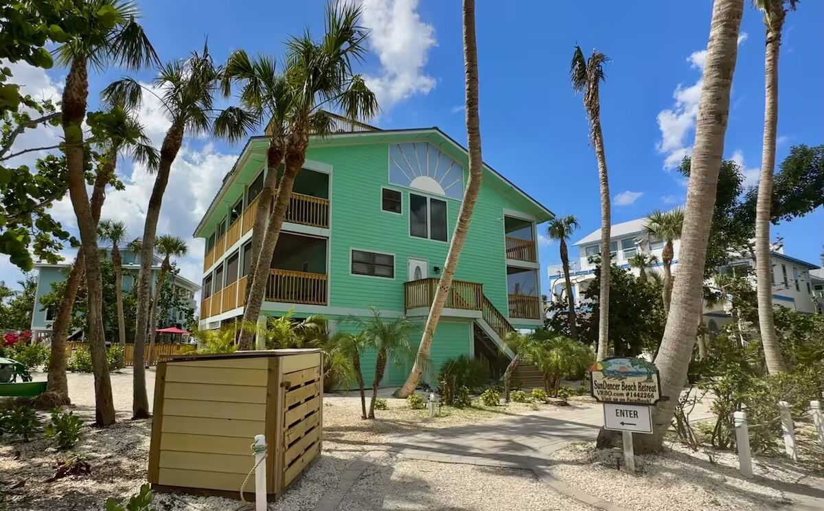 A two-story building with a green facade, a balcony, and a sign indicating a beach retreat.