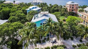 A coastal property with multiple buildings, including a prominent turquoise house with a balcony, surrounded by lush greenery and palm trees. - Private Beach Access Steps Away,  Pool, Outdoor Bar, 2 Golf Carts, 360 Views. (Captiva)
