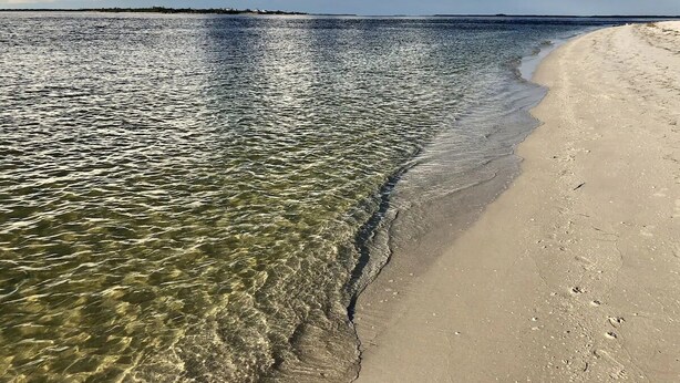 A beach with clear shallow waters, a sandy shore, and a distant landmass under a partly cloudy sky. - Private Beach Access Steps Away,  Pool, Outdoor Bar, 2 Golf Carts, 360 Views. (Captiva)