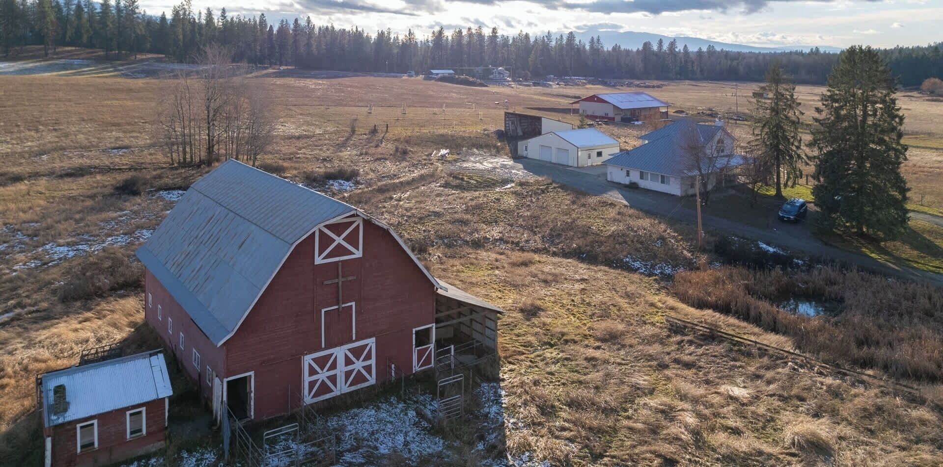 A rural landscape with a red barn, a white building, and a road.