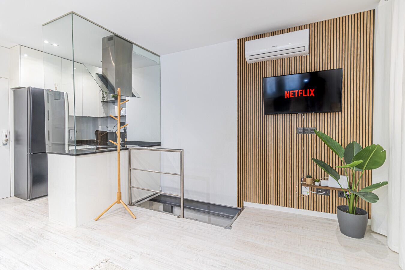Una cuina moderna amb forn integrat, un separador de vidre i una paret de fusta amb un televisor penjat que mostra 'NETFLIX'.