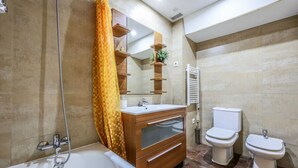 Une salle de bain moderne comprenant une baignoire, un meuble-lavabo avec un miroir, deux toilettes et une douche.