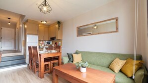 Een moderne keuken met houten kastjes, een eettafel met stoelen, een groene bank en een houten salontafel.