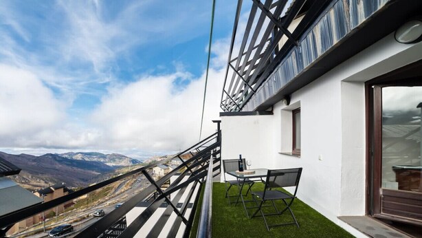 Een balkon met uitzicht op bergen, een tafel met stoelen en een glazen deur.