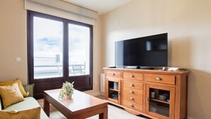 Een woonkamer met een groot raam, een flatscreen televisie, een houten kast en een kleine tafel met een plant.