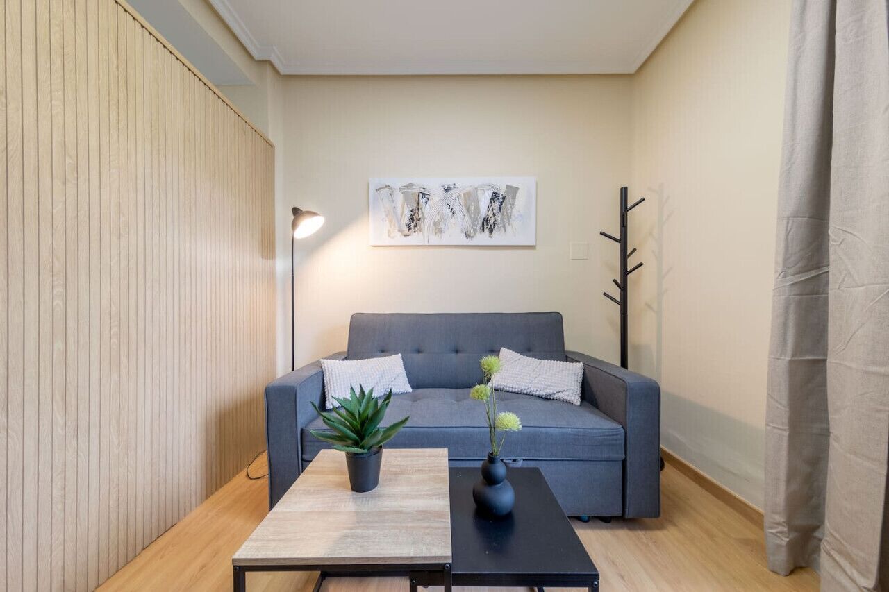 A modern living room with a grey sofa, two black coffee tables, a potted plant, and a wall-mounted abstract art piece.