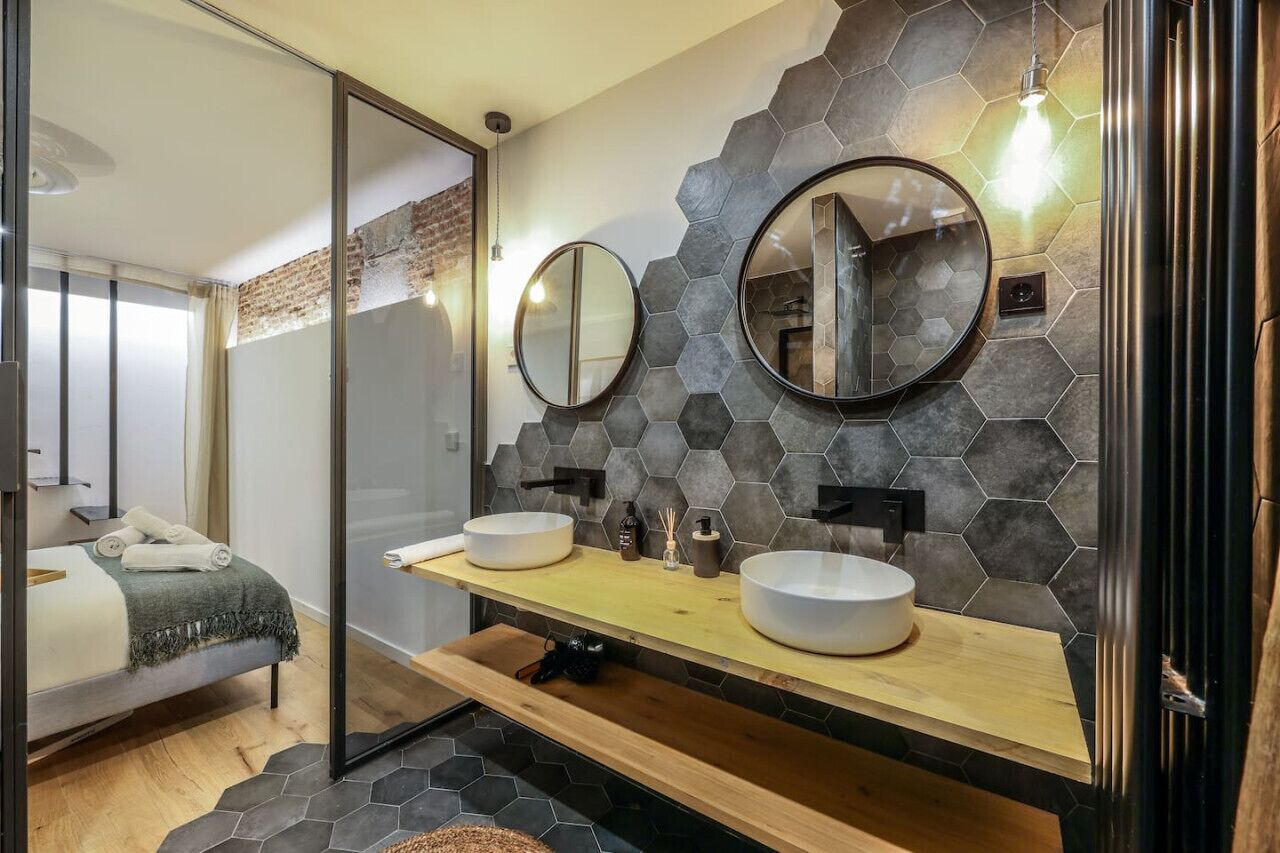 Une salle de bain moderne avec deux miroirs ronds, un meuble-lavabo en bois et un pare-feu en carreaux hexagonaux.