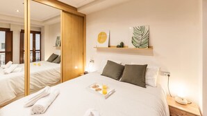 A hotel room with a large mirror, a bed with a tray of breakfast, and a shelf with a plant and a framed picture.