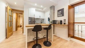 A modern kitchen with white cabinets, a stainless steel range, and a black countertop. There are two black bar stools under the counter. A sign on the wall reads "LOVE YOU BACK."