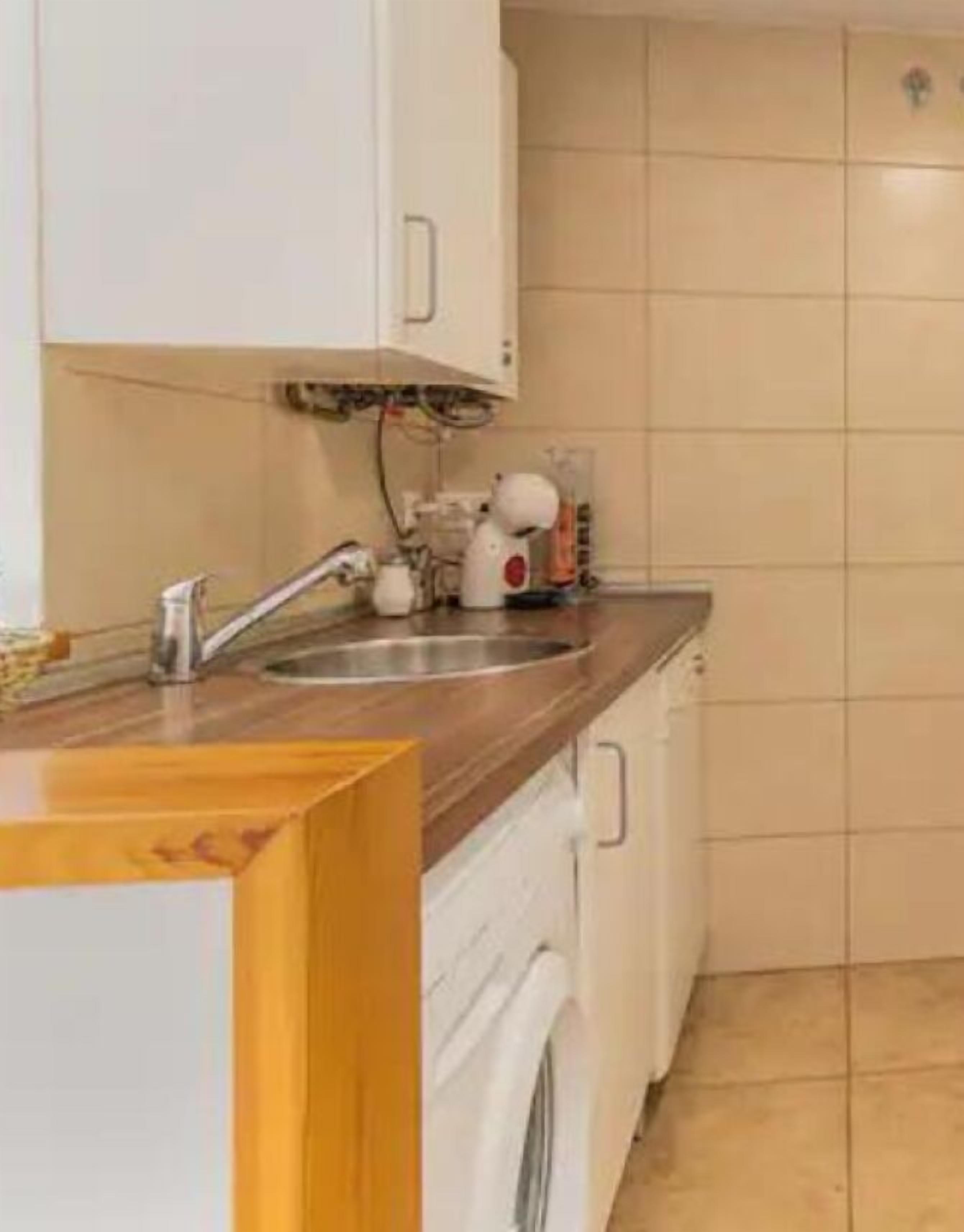Una cocina con encimera de madera, un lavamanos, una lavadora y salpicadero de azulejos.
