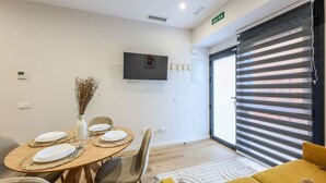 A modern dining area with a round table set for four, a flat-screen TV mounted on the wall, and a sliding glass door with blinds. - Luxe Apartments Madrid Rio by Rentitup (Madrid)
