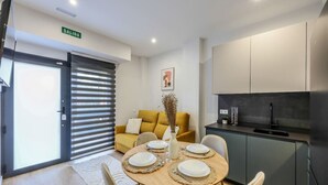 A modern kitchen with a black countertop and a sink. There is a yellow sofa with a white cushion in the living area. A dining table with white plates and silverware is set up in the center. - Luxe Apartments Madrid Rio by Rentitup (Madrid)
