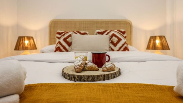 A neatly made bed with a wooden headboard, two pillows with a geometric pattern, a tray with croissants and a red mug, and two lamps on either side of the bed. - Luxe Apartments Madrid Rio by Rentitup (Madrid)