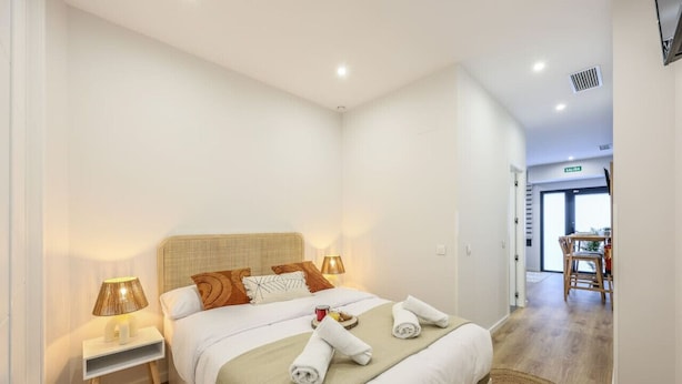 A hotel room with a bed, bedside lamps, a small table, and a view of the hallway. - Luxe Apartments Madrid Rio by Rentitup (Madrid)