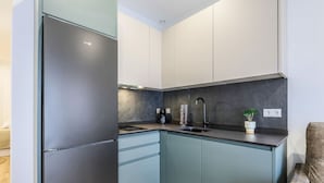 A modern kitchen with a stainless steel refrigerator, light blue cabinets, a black countertop, and a small potted plant. - Luxe Apartments Madrid Rio by Rentitup (Madrid)