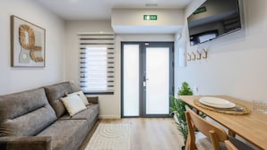 A modern living room with a sofa, a dining table with chairs, a TV mounted on the wall, and a sliding glass door leading to the outside. - Luxe Apartments Madrid Rio by Rentitup (Madrid)