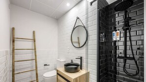 A modern bathroom with a toilet, a wooden vanity with a black sink, a glass shower enclosure, and a bamboo ladder. - Luxe Apartments Madrid Rio by Rentitup (Madrid)