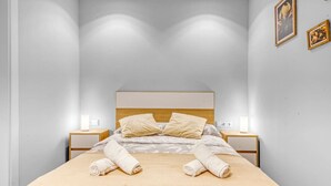 A neatly made bed with two pillows, two bedside tables with lamps, and a wall with two framed pictures.