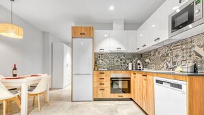 A modern kitchen with white cabinets, a wooden countertop, a patterned backsplash, and a dining area with a white table and chairs.
