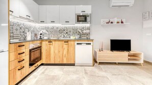 A modern kitchen with white cabinets, a microwave, a dishwasher, and a TV on a wooden stand.