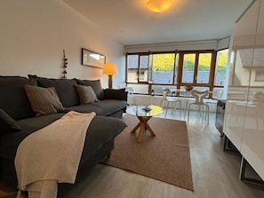A modern living room with a sofa, a coffee table, and a dining area with chairs and a table.