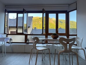 A room with large windows, a table with chairs, and a view of a mountain.