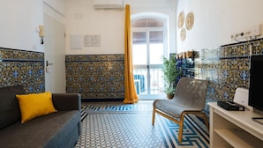 A room with patterned tile walls, a sofa with a yellow pillow, a chair, a television, and a potted plant. - Andalusian Flavour in Heart of Seville 4´giralda (Sevilla)