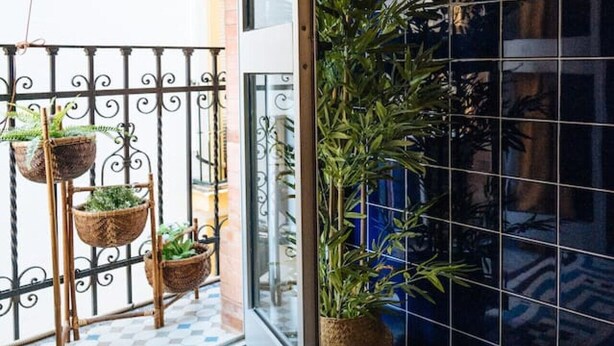 A balcony with wicker planters and a potted plant, a tiled floor with a geometric pattern, and a blue-tiled wall with woven decorations. - Andalusian Flavour in Heart of Seville 4´giralda (Sevilla)