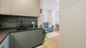 A modern kitchen with grey cabinets, a black countertop, and a marble backsplash. There is a small potted plant on the counter.