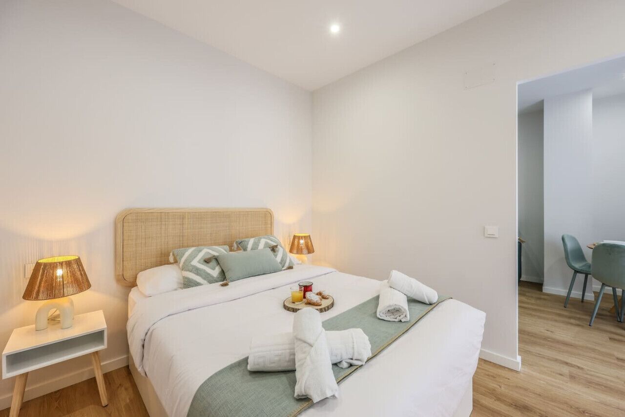 A neatly made bed with pillows, a bedside table with a lamp, and a tray with breakfast items.