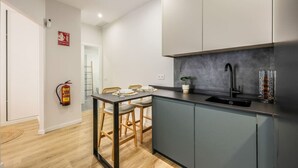 A modern kitchen with grey cabinets, a black countertop, and a stainless steel sink. There is a fire extinguisher mounted on the wall and a small potted plant on the counter. - Luxe Apartments Madrid Rio by Rentitup (Madrid)