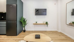 A modern kitchen with a built-in refrigerator, a flat-screen TV mounted on the wall, and a small wooden shelf with decorative items. - Luxe Apartments Madrid Rio by Rentitup (Madrid)