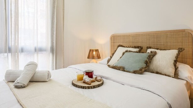 A neatly made bed with a tray of breakfast items, a lamp, and a window with sheer curtains. - Luxe Apartments Madrid Rio by Rentitup (Madrid)