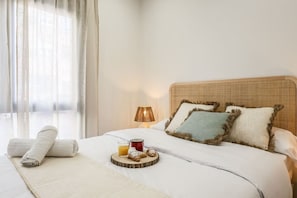 A neatly made bed with a tray of breakfast items, a lamp, and a window with sheer curtains.