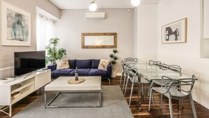 Moderni olohuone, jossa on televisio, sohva, sohvapöytä sekä ruokailutila tuoleineen ja lasipöytineen.