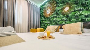 Hotellihuone, jossa on sänky, aamiaistarjotin, jossa on kuppi ja lasi mehua, sekä trooppiseen teemaan sopiva seinämaalaus.