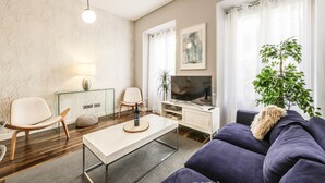 Moderni olohuone, jossa on sohva, sohvapöytä, televisio ja huonekasvi.