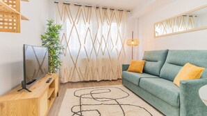 A living room with a green sofa, a TV on a wooden stand, a plant, and a patterned rug.