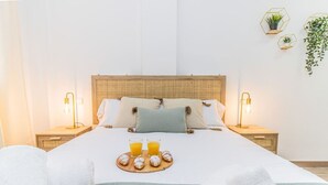 A neatly made bed with a tray of pastries and orange juice, two bedside lamps, and a wall-mounted plant.