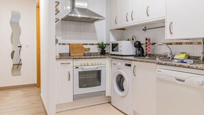 A modern kitchen with white cabinets, a built-in oven, a microwave, and a washing machine.