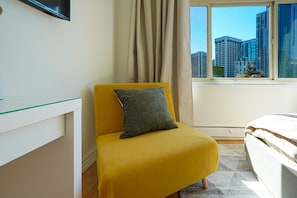 A room with a yellow armchair, a bed, a glass table, and a window with a city view. - Downtown Studio with King Bed & City Views (Seattle)