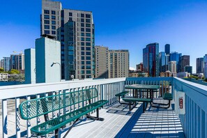 A rooftop terrace with green metal benches and a table, overlooking a cityscape with modern buildings. - Downtown Studio with King Bed & City Views (Seattle)