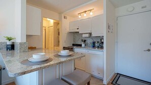 A compact kitchen with white cabinets, a granite countertop, and a built-in oven. - Downtown Studio with King Bed & City Views (Seattle)