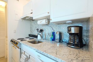 A kitchen with a stove, sink, coffee maker, and cabinets.